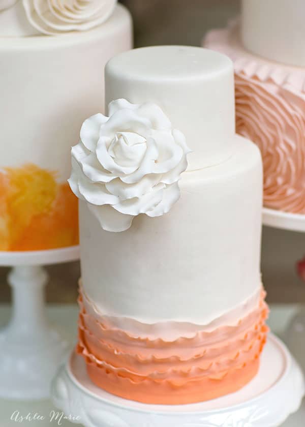 the smallest of the three cakes is simply beautiful with a double barrel base with ombre ruffles topped with a gumpaste white rose